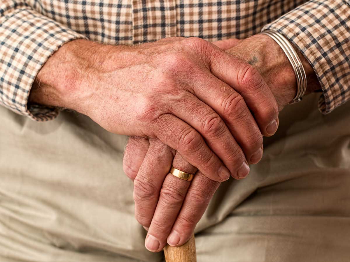 Mão de uma pessoa idosa segurando um apoio de caminhada